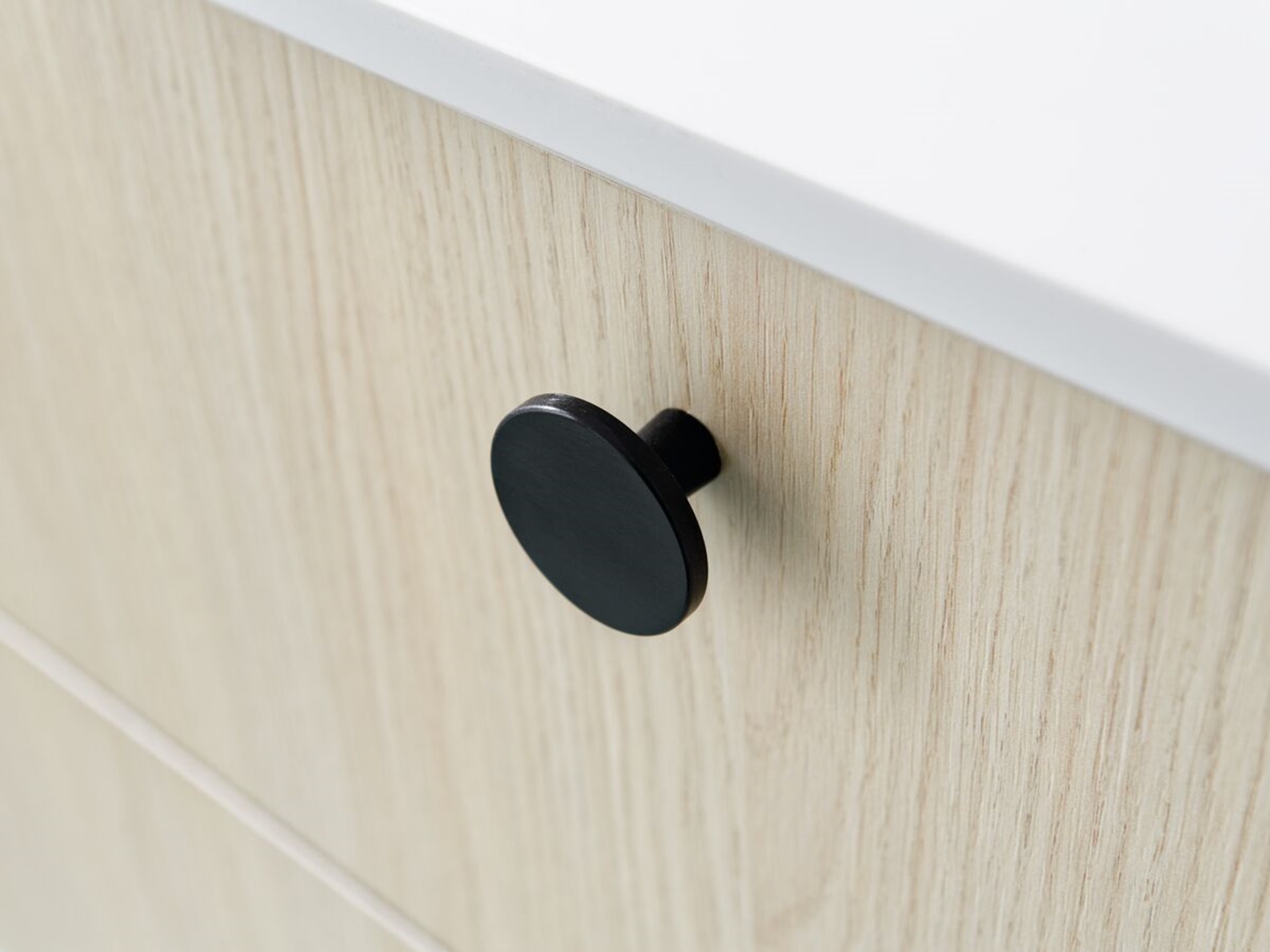 Zoom sur un bouton noir dans un tiroir d'un meuble de salle de bains en bois clair.